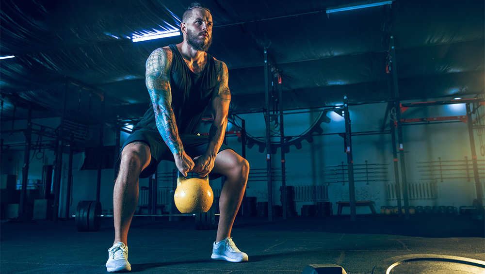 muscular guy with tattoos doing kettle ball swings with a yellow kettle ball