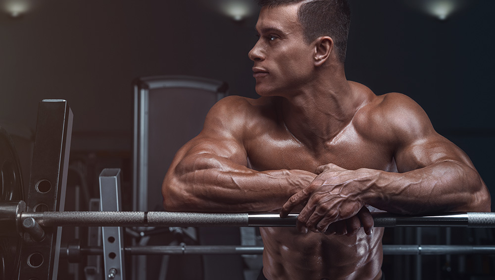 Muscular Tan Guy Leaning on a Barbell at the Gym